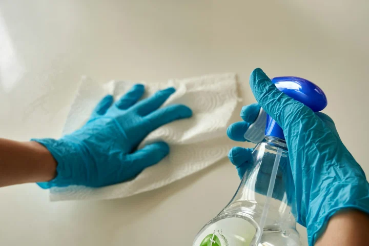 Gloved hands deep cleaning a surface with spray and a cloth